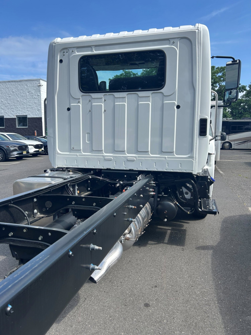 Truck cab rear and chassis showing ROPS, white cab, black chassis rails, exhaust pipe, and rear window.