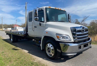 Tow truck front three-quarter view showing cab and flatbed, white exterior, Hino L6 badge not visible, chrome bumper and grille, dual rear wheels.