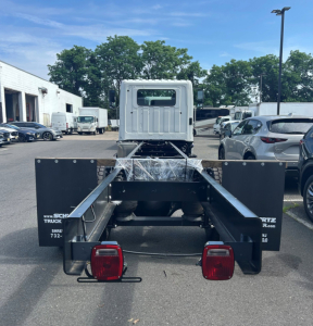 Rear view of a 2025 Hino L6 tow truck chassis showing dual rear fenders, taillights, heavy-duty frame, and cab in background.