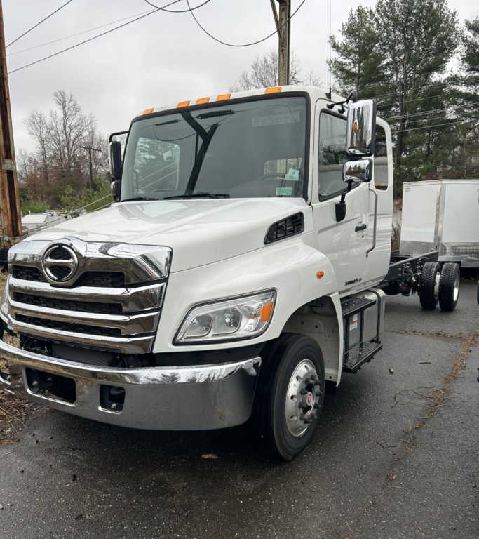 Hino L6 cab chassis truck front view showing white cab and chrome grille with Hino emblem, headlights, side mirrors, and front bumper.