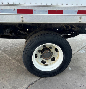 Wheel and side of a 2018 Hino 155 box truck showing a white steel wheel with black tire and wheel hub, undercarriage and reflective tape above the wheel