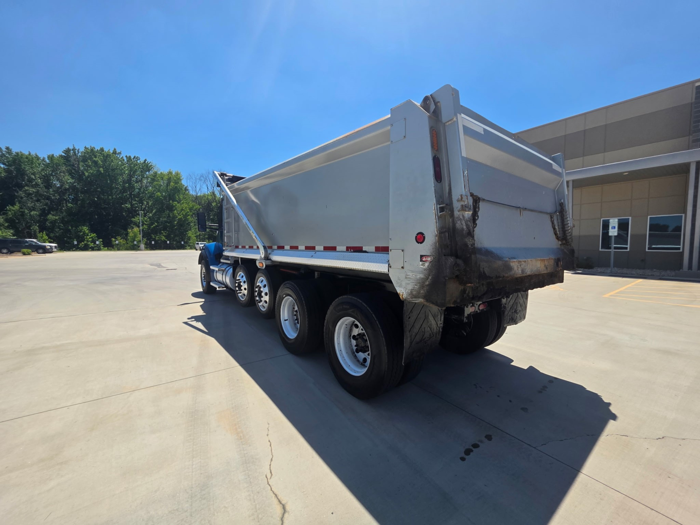 Kenworth T880S dump truck rear-side view showing dump bed and triple-axle rear with silver wheels.