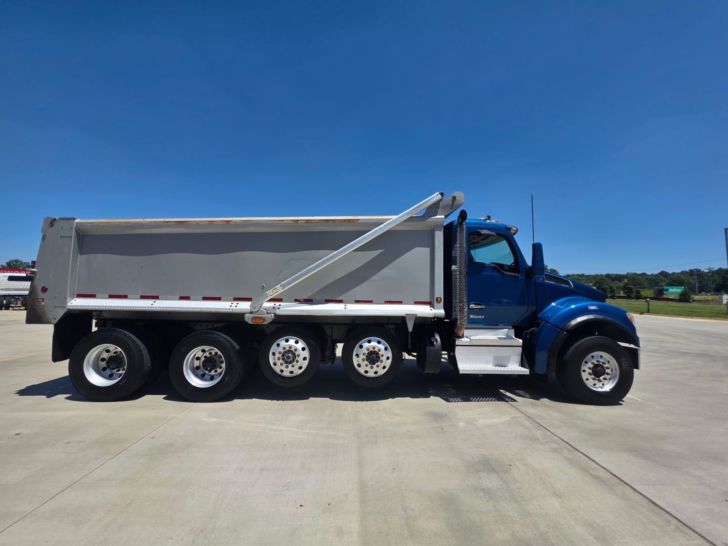 Kenworth T880S dump truck side view showing large metal dump bed, six rear wheels, blue cab, and chrome steps.