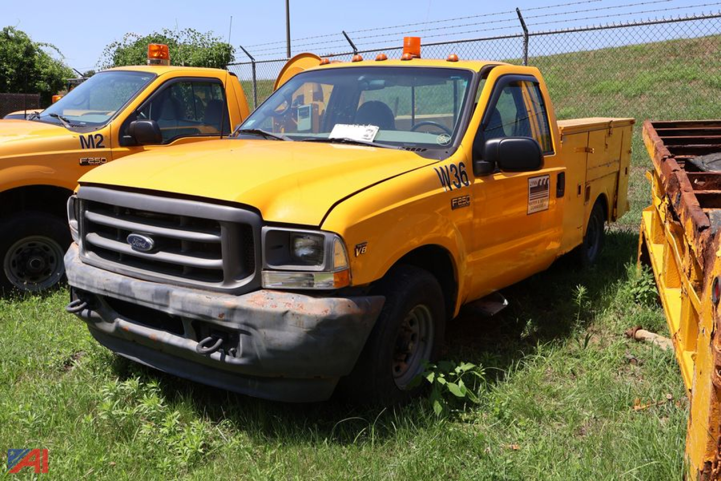 Ford F-250 Super Duty utility truck in yellow with utility bed, front bumper dented, parked on grass next to another yellow service truck.