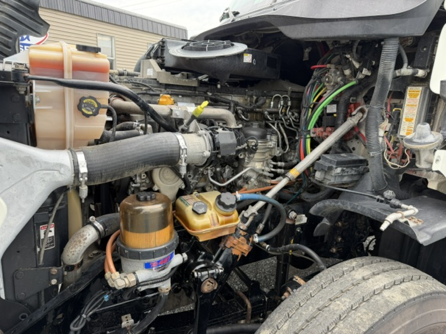 Engine bay of a Freightliner Cascadia CA125DC showing coolant reservoir, hoses, wiring, and turbo/intercooler components visible.