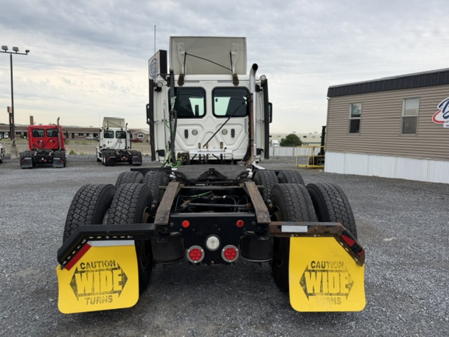 Truck chassis rear view showing fifth wheel area and yellow mud flaps with CAUTION WIDE TURNS markings.