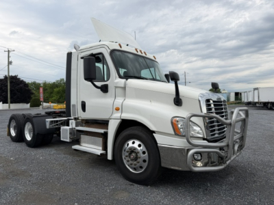 Truck cab and front end of a white Freightliner Cascadia CA125DC truck with grille guard, dual rear axles, side steps, and sun visor.
