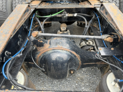 Rear-view of a Freightliner Cascadia chassis showing drive axle housing and suspension components with visible hydraulic hoses and wiring harnesses.