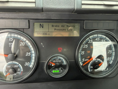 Freightliner Cascadia dash panel showing gauges: left tachometer, center DEF/low pressure indicator, right speedometer; digital message reads 'Brake Air Supply Pressure Low' with N gear indicator.