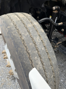 Wheel and suspension of a Freightliner Cascadia front axle with treaded tire, visible shock absorber and components.