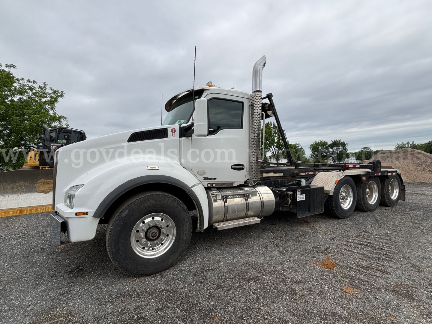 Kenworth T880 roll-off truck in white, side view showing cab and chassis with dual rear axles and chrome exhaust stack.