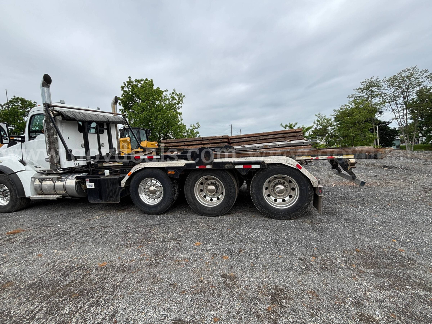 Kenworth T880 roll-off truck side view showing flatbed with stacked rails and dual rear axles.