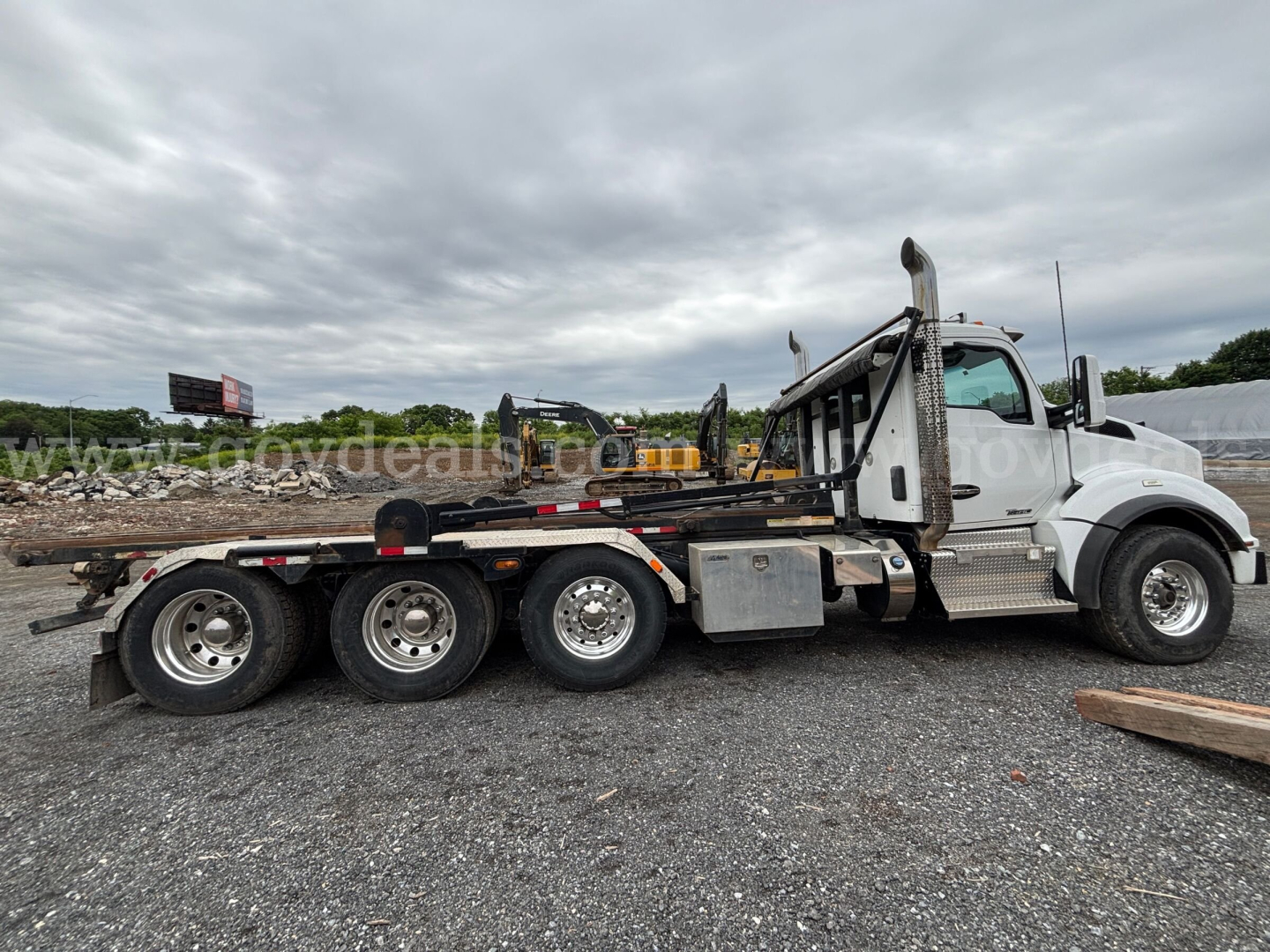 Kenworth T880 rollover truck side view showing five-wheel? tandem rear axles with flatbed/roll-off body and silver fuel tank; cab with white paint and chrome steps.