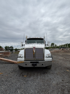 Front view of a white 2016 Kenworth T880 roll-off truck showing grille, bumper, and headlights with large chrome bumper and Kenworth emblem.