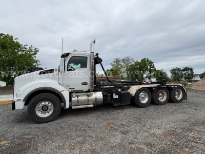 Kenworth T880 rolloff truck with white cab and long wheelbase, side view showing fuel tanks and exhaust stack.