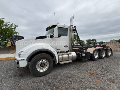 Kenworth T880 roll-off truck in white, side view showing cab and chassis with dual rear axles and chrome exhaust stack.