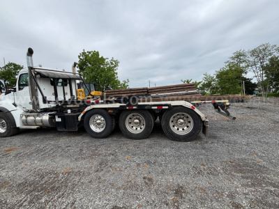 Kenworth T880 roll-off truck side view showing flatbed with stacked rails and dual rear axles.