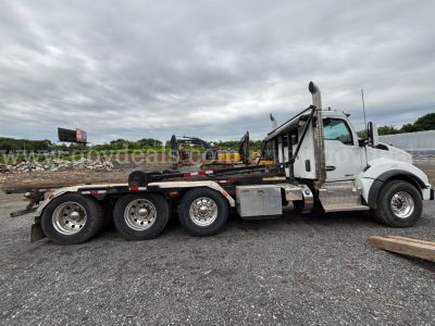 Kenworth T880 rollover truck side view showing five-wheel? tandem rear axles with flatbed/roll-off body and silver fuel tank; cab with white paint and chrome steps.