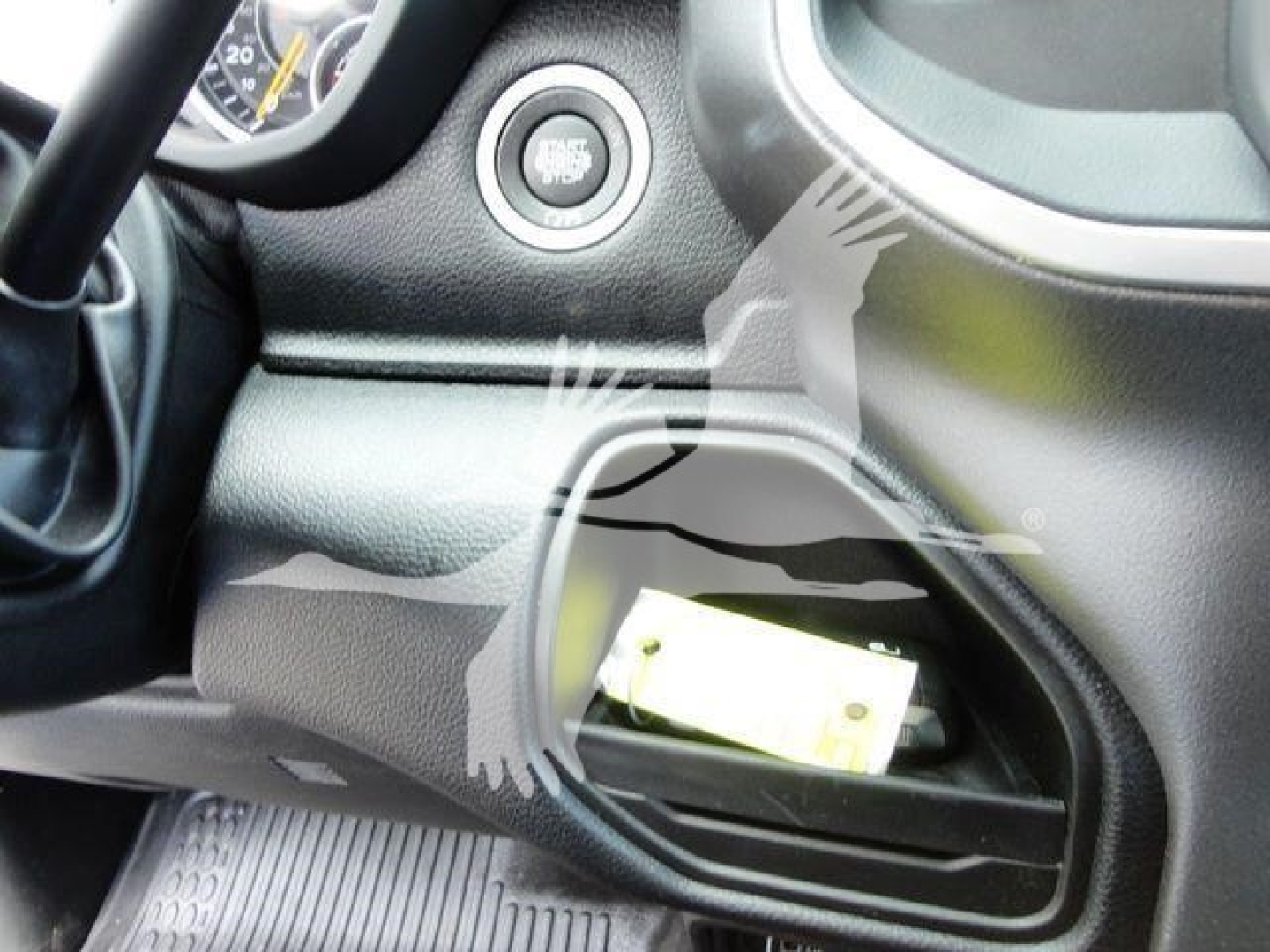 Vehicle interior showing a push-to-start button and a storage pocket with a rectangular yellow label or card partially visible.