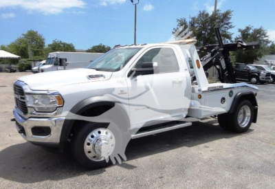 Ram 4500 tow truck with winch and tow equipment, white cab and flatbed, side view showing wheel, chrome grille and towing apparatus.