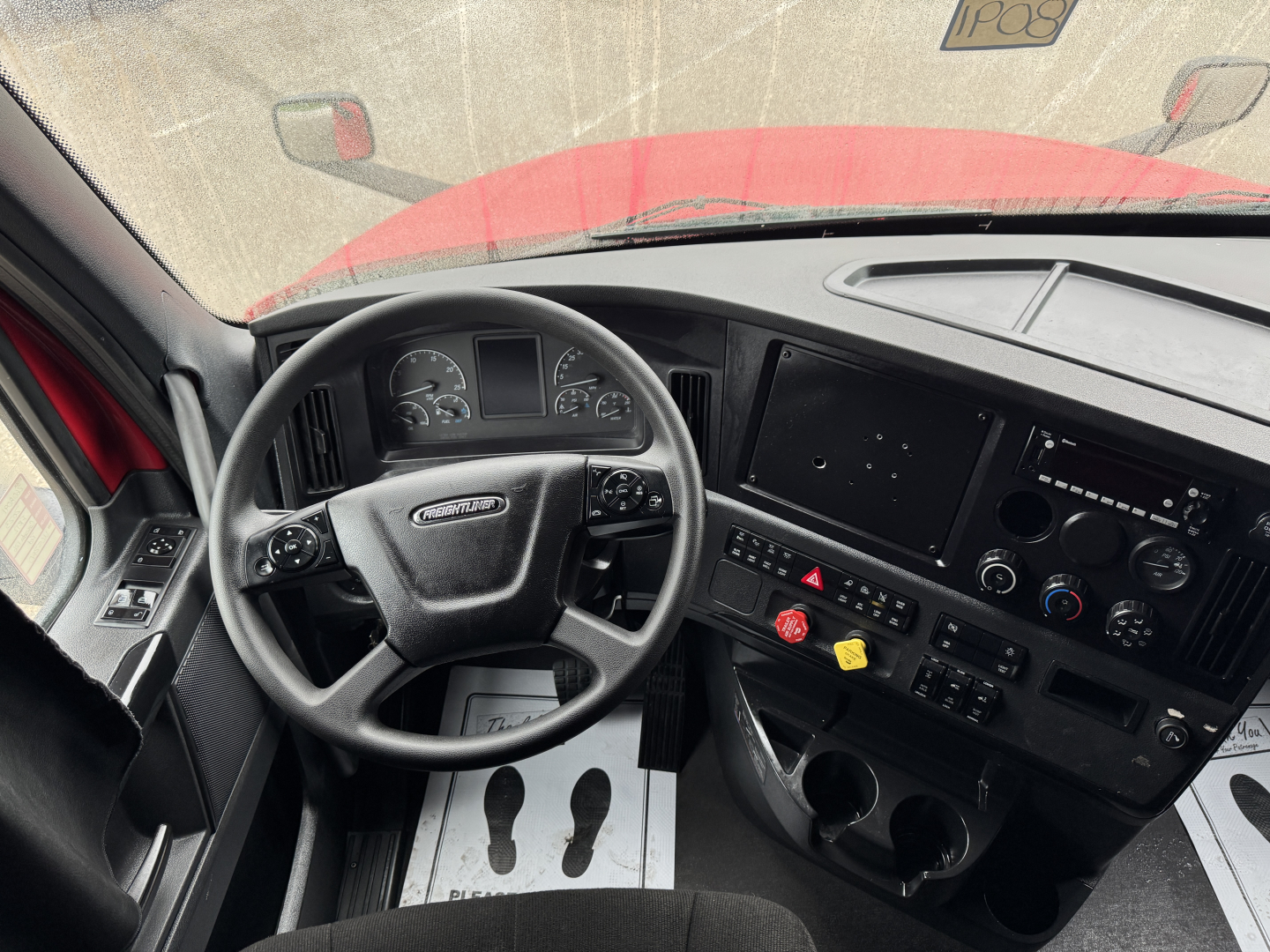 Cab of a Freightliner Cascadia 126 truck showing steering wheel, dashboard with gauges, control panel, and two cup holders near center console.