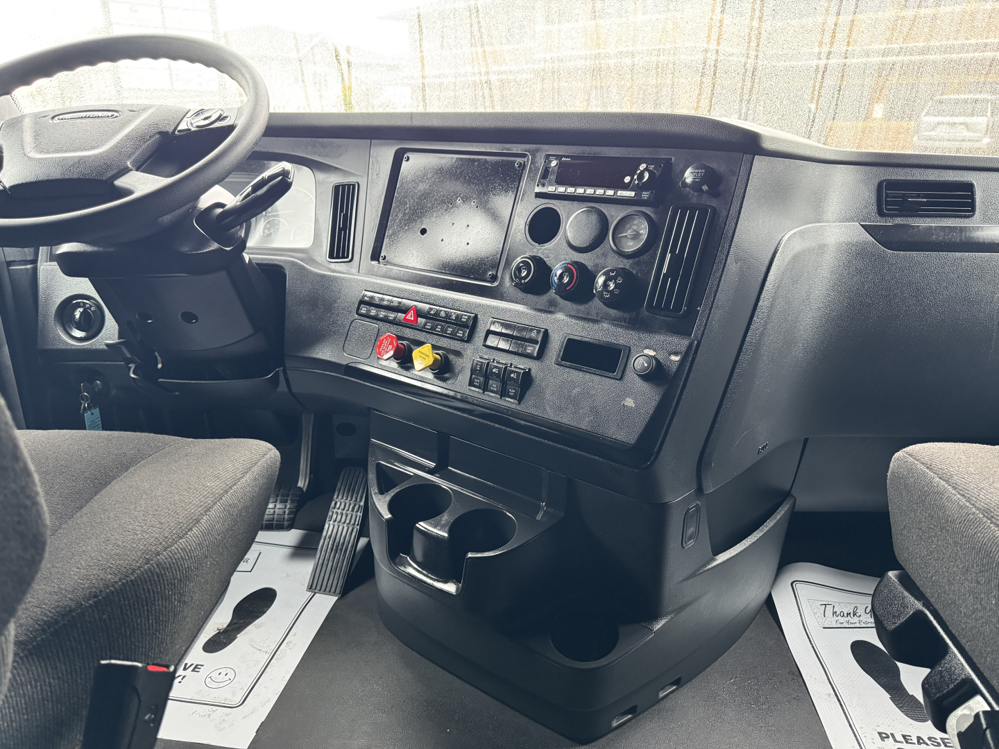 Cab interior of a Freightliner Cascadia 126: dashboard with steering wheel, center console, multiple controls, cup holders, and driver/passenger seats.