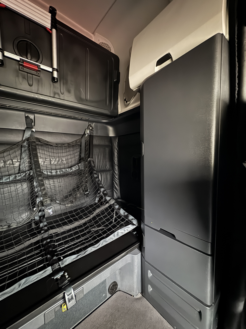 Cabin sleeper area of a 2023 Freightliner Cascadia 126 showing storage nets, cabinet doors, and side panel with compartments.