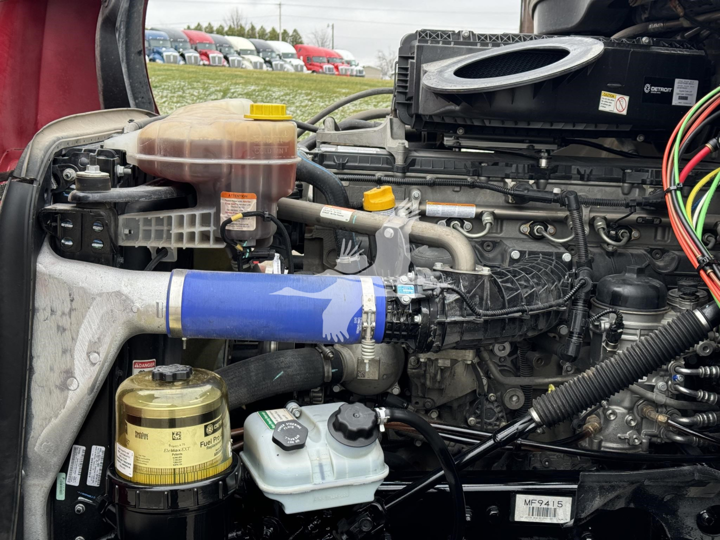 Freightliner Cascadia 126 engine bay showing coolant reservoir, oil filter, and various hoses and wiring in view.