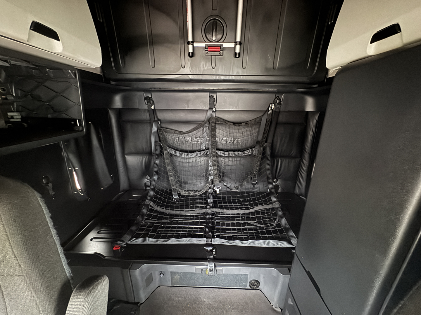 Freightliner Cascadia sleeper cab interior showing storage net with mesh, cargo area, and overhead panels; cabin light and tie-downs visible.