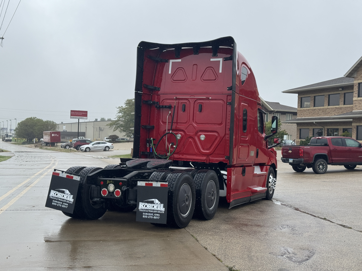 Truck chassis and rear of a red Freightliner Cascadia 126 tractor, view from the left-rear showing rear wheels and mudflaps with Kordell trailer dealership text.