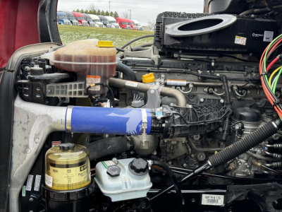 Freightliner Cascadia 126 engine bay showing coolant reservoir, oil filter, and various hoses and wiring in view.