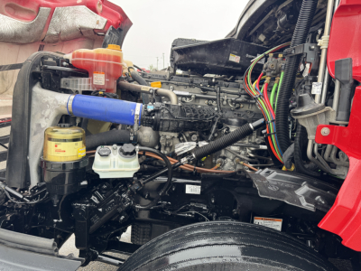 Truck engine bay of a 2023 Freightliner Cascadia 126 showing engine components, hoses, wiring harness, coolant reservoir, and hydraulic lines.