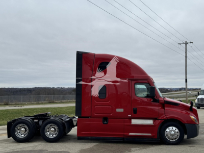 Freightliner Cascadia 126 tractor, red cab, side view showing sleeper, two rear axles, white decals on door.