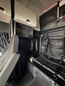 Freightliner Cascadia cab interior showing sleeper area with netting, overhead storage, and control panels.