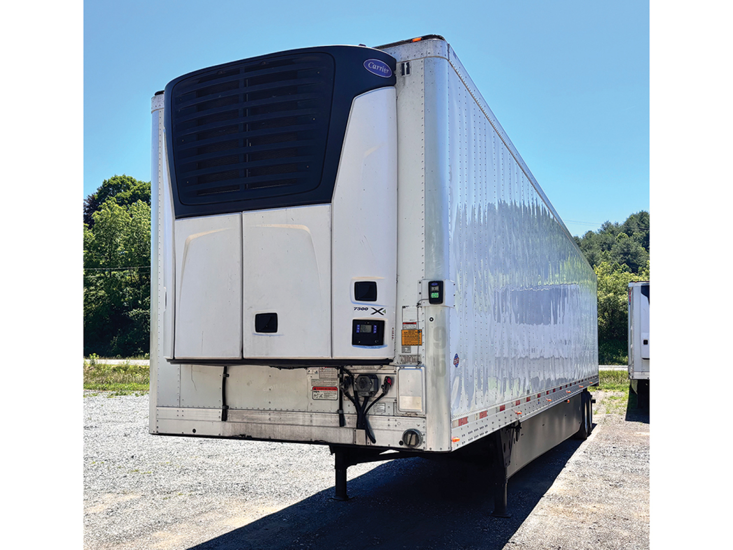 Utility 3000R refrigerated trailer with rear refrigeration unit and white body, dock bumper, blue sky background, on gravel lot.