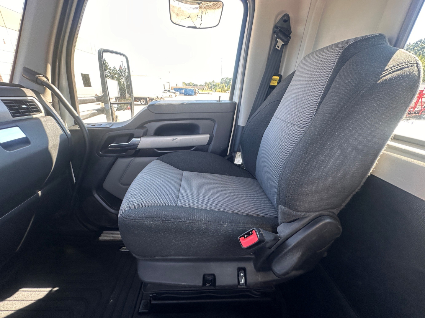 Kenworth T880 cabin seat and interior view showing front passenger seat with seatbelt buckle, door panel, and dashboard in a daytime showroom setting.