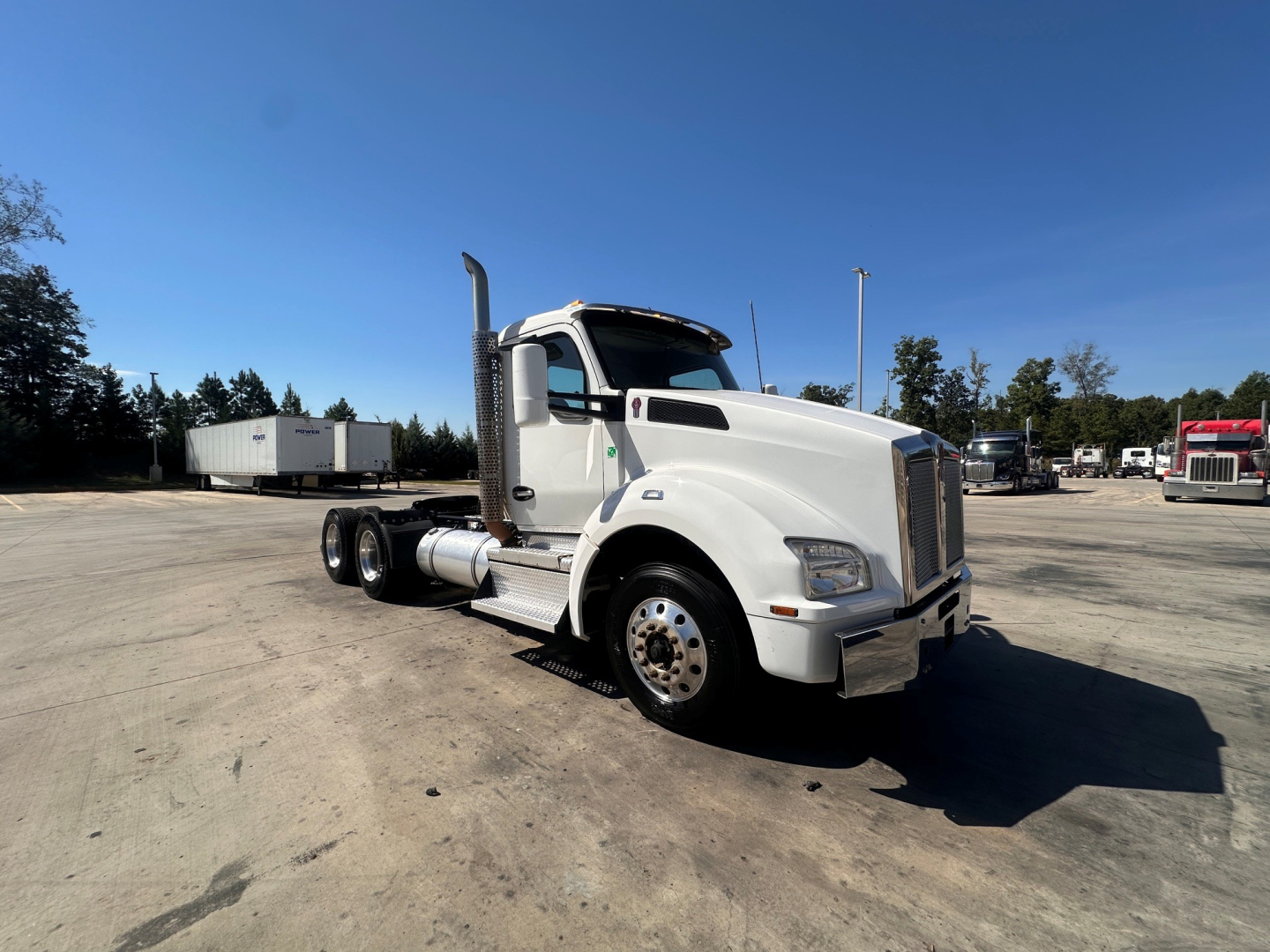 Kenworth T880 conventional daycab truck in white with dual rear axles and chrome exhaust stack, front grille, and large side mirrors.