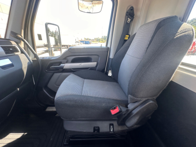 Kenworth T880 cabin seat and interior view showing front passenger seat with seatbelt buckle, door panel, and dashboard in a daytime showroom setting.