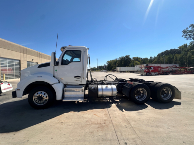 Kenworth T880 daycab tractor rear cab view showing fuel tanks and drive axles with 3 rear wheels and black chassis.