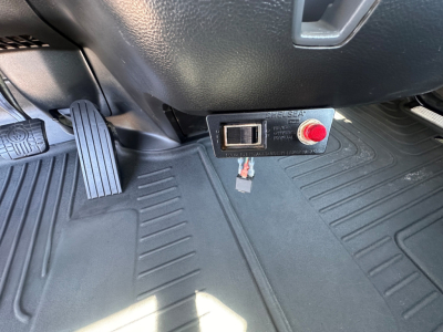 Kenworth T880 cab interior showing Elsea electronic control unit and red pushbutton near floor mat under dash.