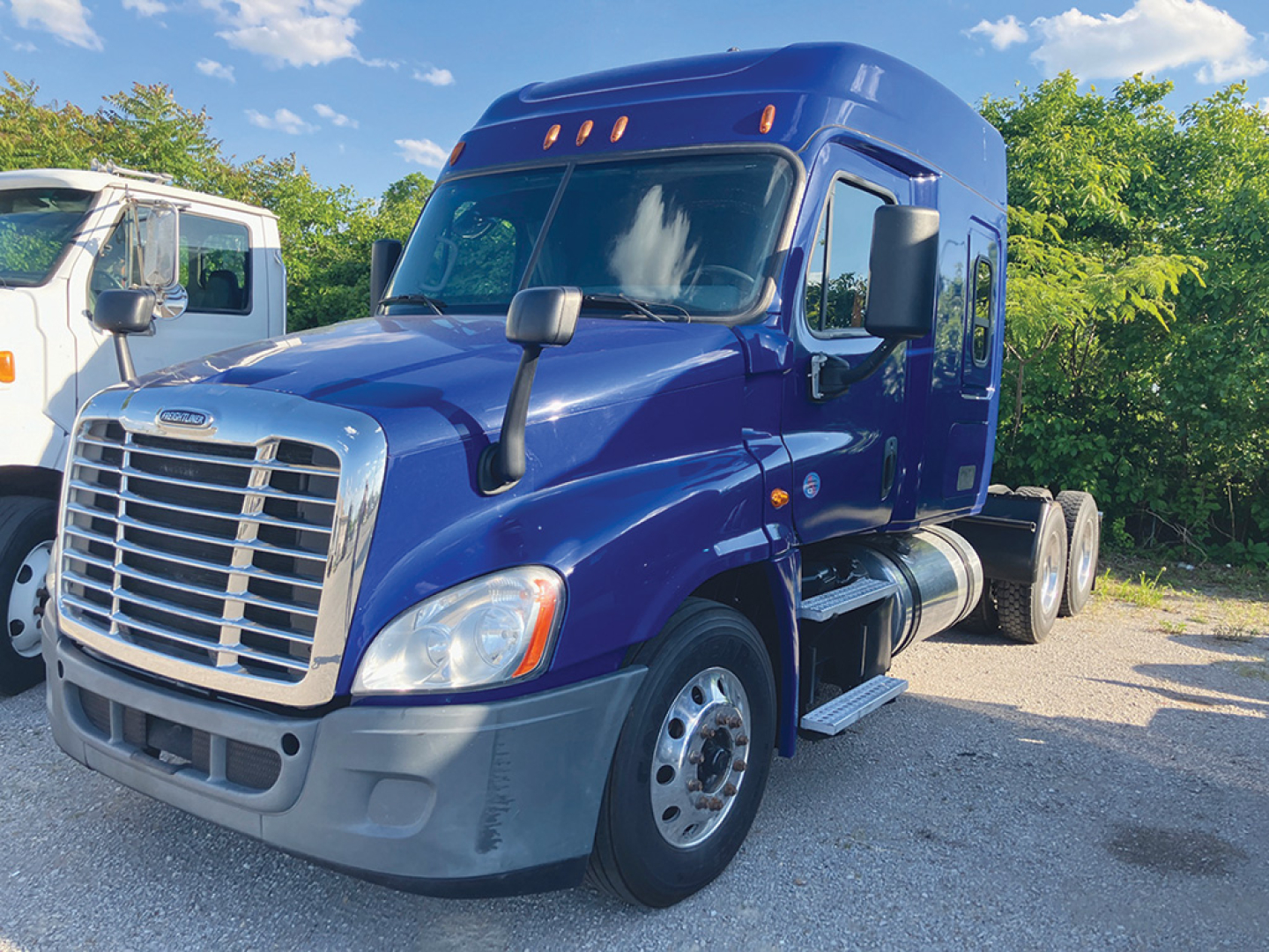 2019 Freightliner Cascadia125 tractor cab in blue, front grille, large mirrors, two fuel tanks, three axles visible, daylight.