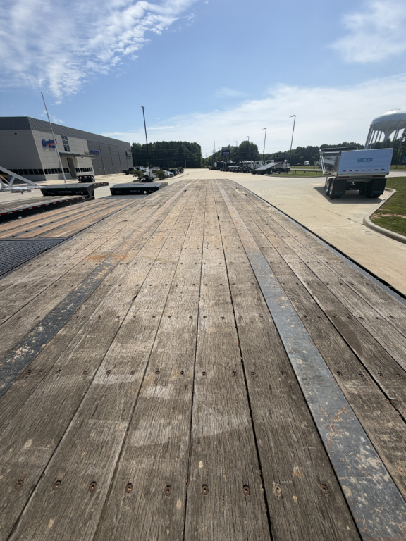 Flatbed trailer deck with wooden planks and metal edge strips, long perspective view toward horizon at industrial lot.