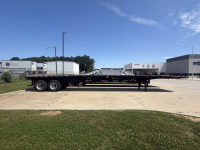  Fontaine HAVSF12SST flatbed trailer with long flatbed and triple axle, side rails, and hydraulic ramps in a dealership lot.