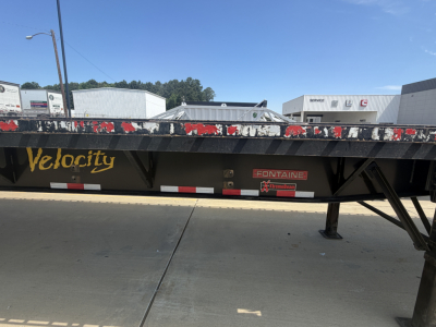 Flatbed trailer side showing Velocity brand and Fontaine HAVSF12SST model details with wear on paint and hitch area.