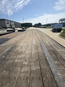 Flatbed trailer deck with wooden planks and metal edge strips, long perspective view toward horizon at industrial lot.