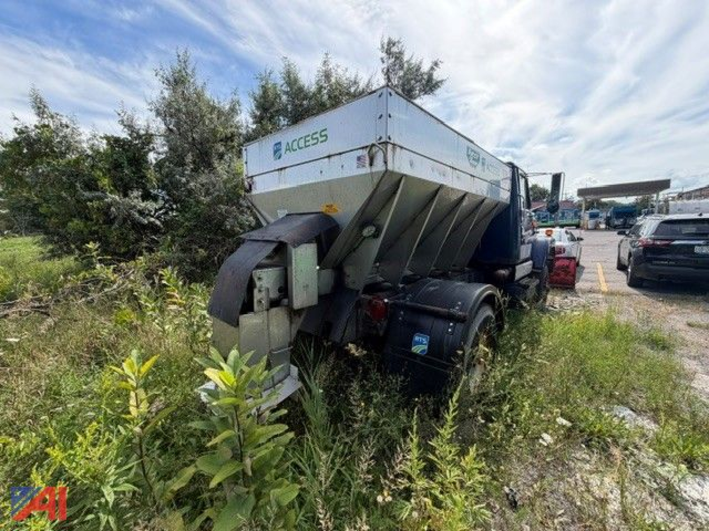 Trailer with stone spreader in overgrowth showing ACCESS and brand markings on the spreader box.