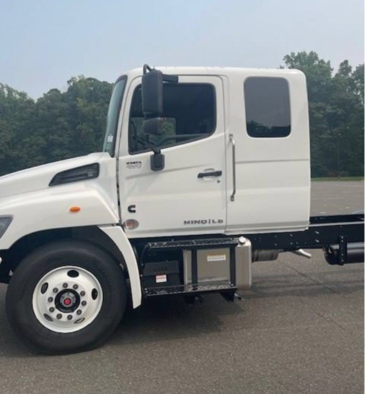Hino L6 cab and chassis truck side view showing white cab, black chassis, and storage box under door; visible wheel and window.