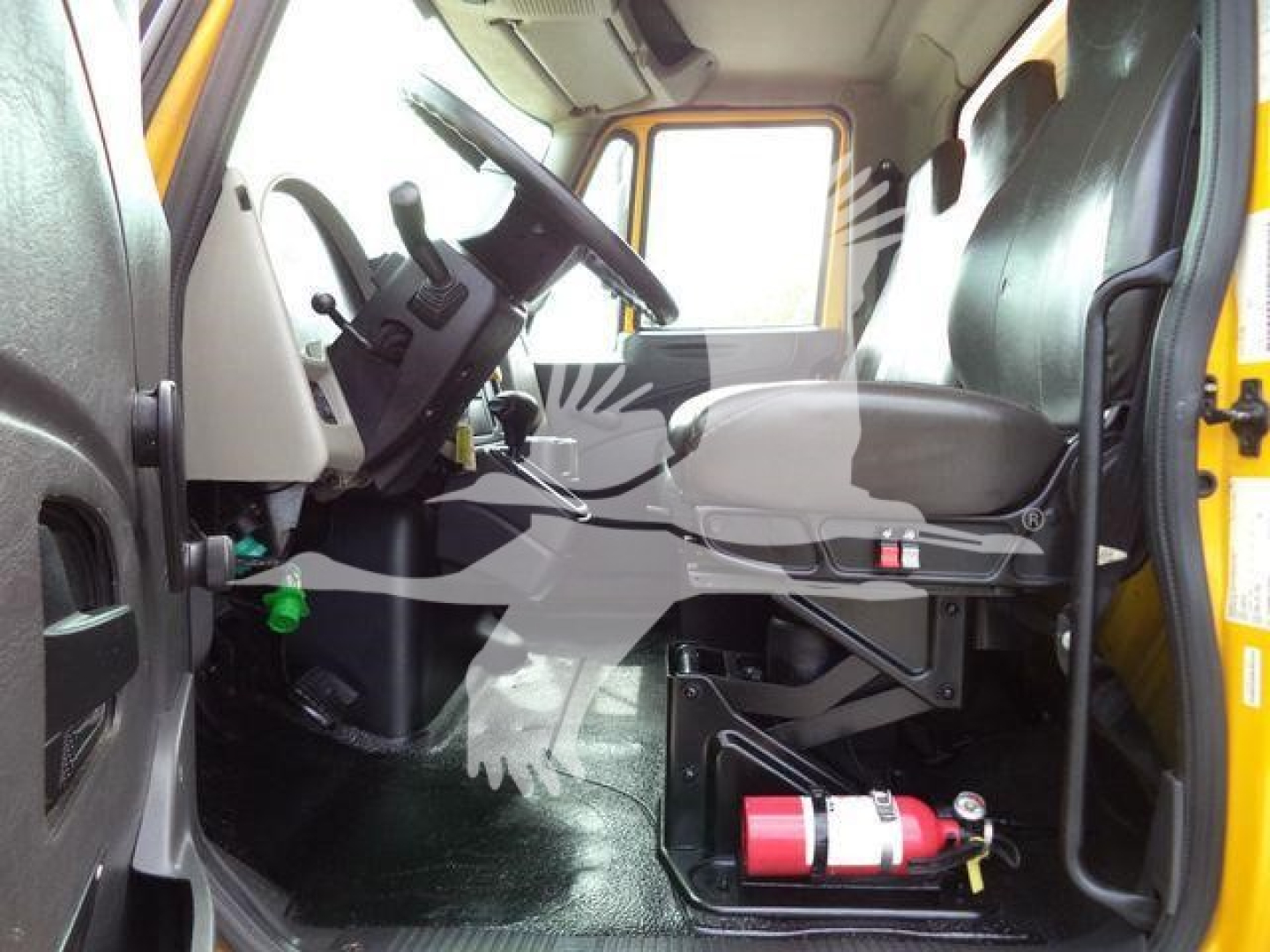 Truck cab interior view of a 2018 International Durastar 4300 showing driver seat, steering wheel, pedal area, and a red fire extinguisher mounted under the dashboard.