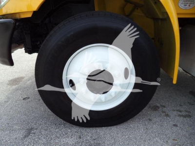 Truck wheel close-up showing black tire mounted on white steel rim with yellow body panel in background.