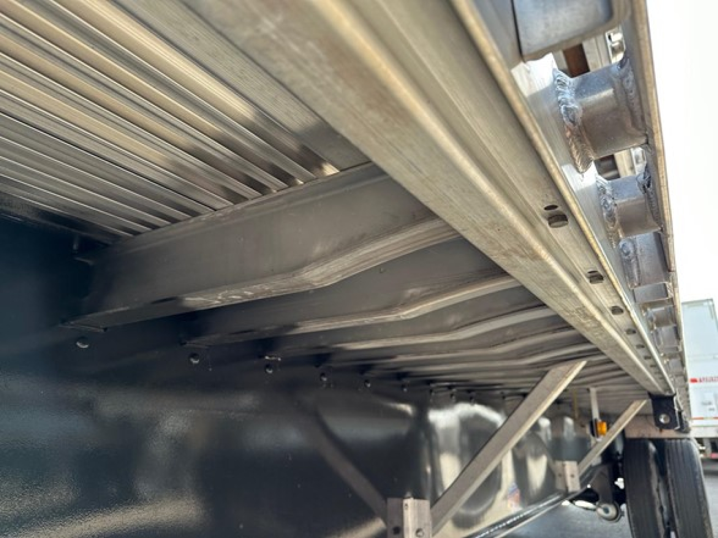 Trailer undercarriage showing steel frame and support beams of a Utility flatbed trailer, view from side with wheel visible and corrugated deck rail.